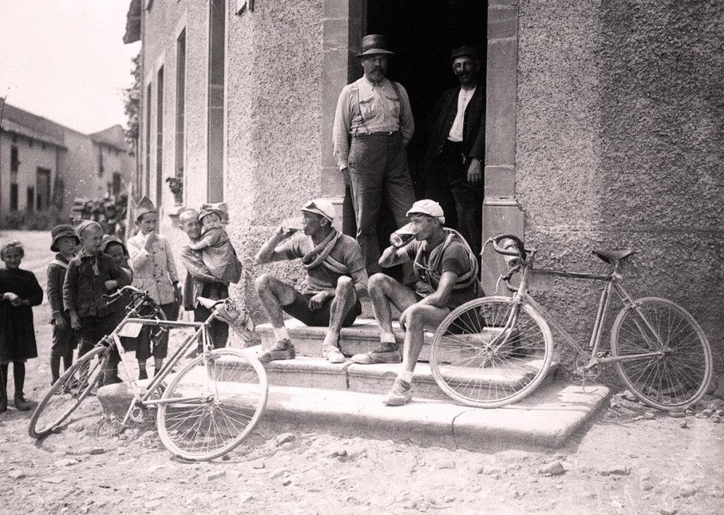 Cyclists having a break, sutting and drinking on the steps of a tavern in 1921